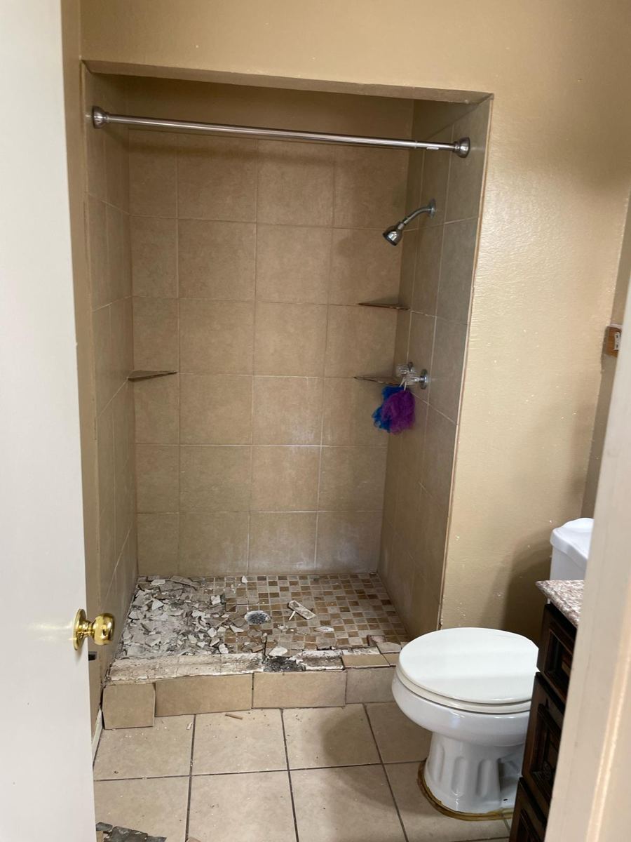 Original beige shower with broken floor tile before remodeling